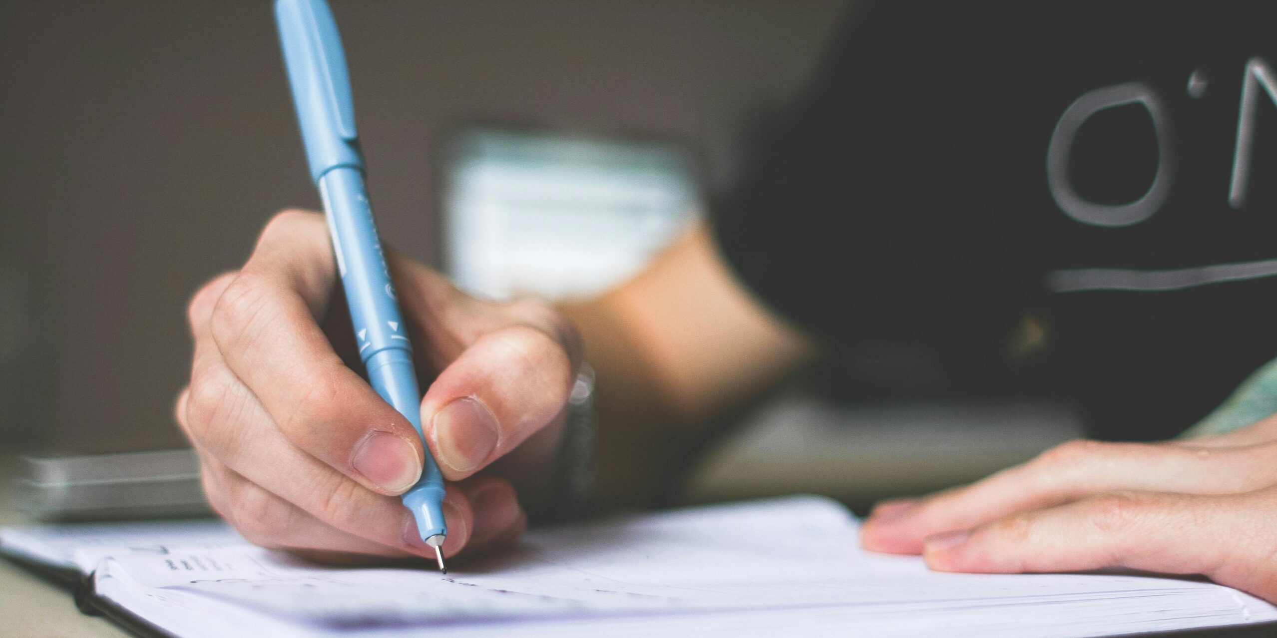 Close-up of hand writing in notebook using a blue pen, focus on creativity.